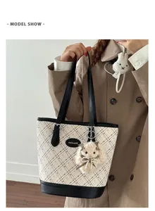 Detail shot of a minimalist plaid tote bag with black leather straps and a plush charm