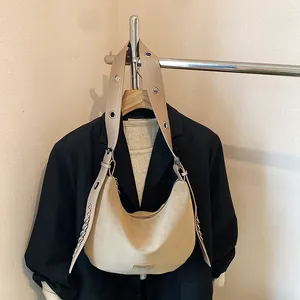 Beige matte hobo bag with eyelet wide strap and chain detail against a black blazer