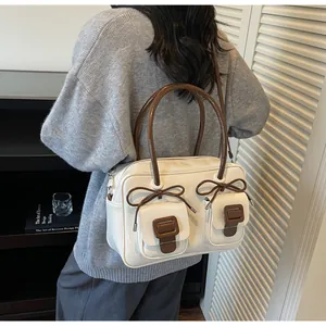 Detail of white leather shoulder bag with brown bow accents and cylindrical handles