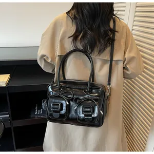 Detailed view of black glossy shoulder bag with bow accents and dual buckle front pockets