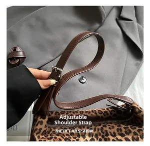 Detail of adjustable dark brown leather strap and metal buckle on leopard print bag
