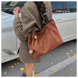 Detail of brown suede tote with laser-cut floral patterns and ethnic tassel charm