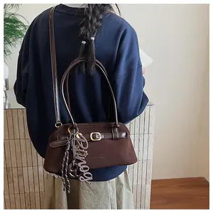 Detail of coffee brown suede bowling bag featuring long strap and letter charm accessory
