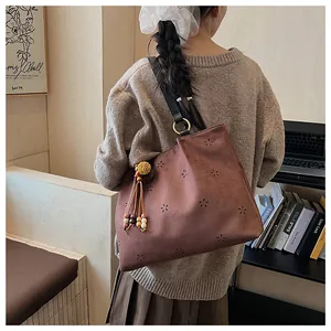 Detail of laser-cut floral pattern and decorative tassel on brown suede hobo bag