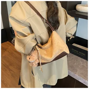 Brown suede hobo bag shown on shoulder with cute plush dog charm in cozy home setting