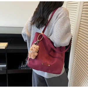 Detail of dark red suede tote bag with plush bear charm and metallic brand tag