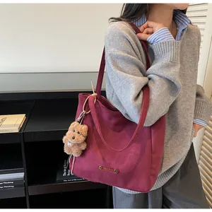 Macro shot of burgundy suede tote bag with brand leather tag and cute brown bear charm