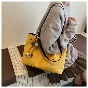 Detail of yellow suede tote bag with hollow flower patterns and ethnic tassel charm