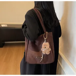 Detail of dark brown faux suede tote bag with metal logo and plush bear charm