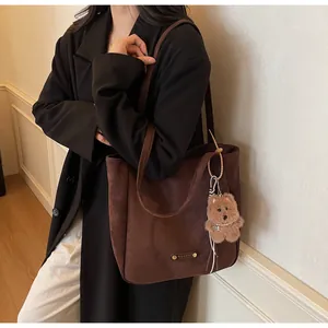 Detail of dark brown suede tote bag with golden logo plate and cute plush bear charm