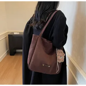 Detail of dark brown suede tote bag with metal plaque and cute bear charm on shoulder
