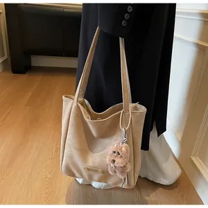 Detail of beige suede tote bag featuring a metal nameplate and a plush teddy charm