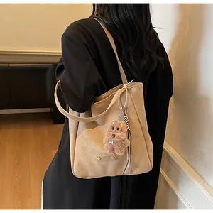 Detail of a brown suede tote bag featuring a cute teddy dog plush charm and metal logo tag