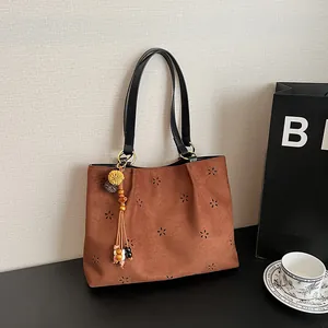 Brown faux suede hobo bag with laser cut floral patterns and ethnic style tassel pendant