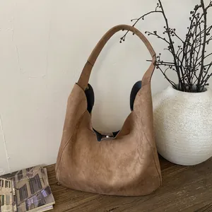 Brown suede hobo tote bag with silver magnetic closure shown in a minimalist setting