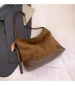 Detailweergave van bruine suède tas met lederen hoekstukken en houten kralenhanger