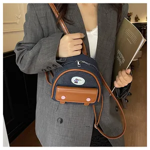 Mini denim backpack with brown leather trim and bear patch worn with a grey blazer