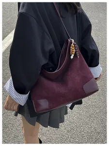 Detail van donkerrode suède hobo tas met vintage kralen en versterkte lederen hoeken