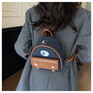 Detail of a mini denim backpack showing brown leather trim and cute bear patch