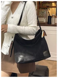 Detail van de zwarte suède hobo tas met lederen hoeken en houten kralen aan een model