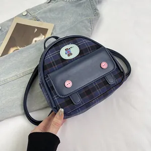 Close-up of blue plaid mini backpack featuring a cute bear patch and pink button accents