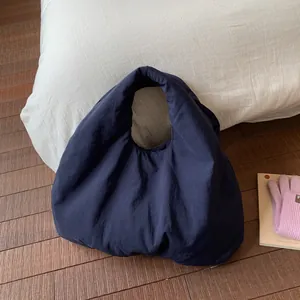 Puffy dark blue pleated tote bag made of soft nylon on a dark wood floor background