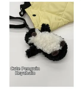 Gros plan d'un pendentif pingouin en peluche attaché à un sac seau jaune matelassé