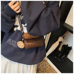 Deep brown cylindrical crossbody bag with plush charm and leather strap on model