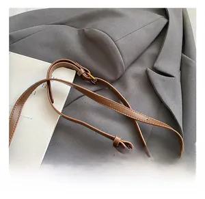 Detail of adjustable brown leather shoulder strap with golden metal buckle and stitching