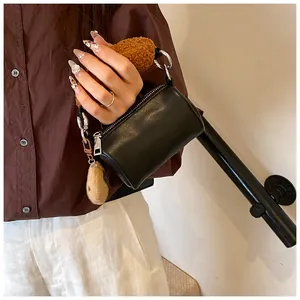 Detail of black cylindrical crossbody bag with brown faux fur handle and silver hardware