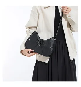 Detail of black crescent shoulder bag with silver studs and ribbon tie on leather texture