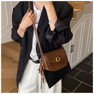 Close-up of brown suede crossbody bag with horseshoe buckle and woven strap detail