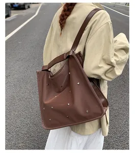 Outdoor street style view of a large brown leather tote bag with silver metal studs
