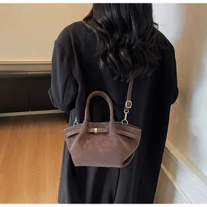 Détail du sac bandoulière vintage en daim marron porté avec un long manteau noir en laine