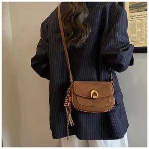 Close-up of brown suede saddle bag with gold horseshoe buckle and long leather tassels