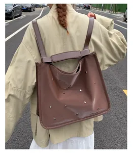 Brown leather tote bag featuring silver heart rivets shown on a shoulder in street style