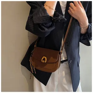 Detail of a brown leather saddle bag with a gold horseshoe buckle and striped tassel charm