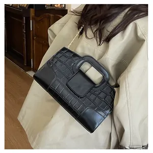 Detail of black crocodile embossed handbag with rectangular handle and gold chain strap