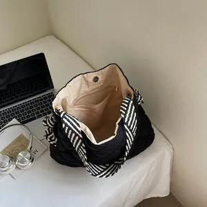 Quilted black tote bag with striped handles and spacious interior shown on white desk