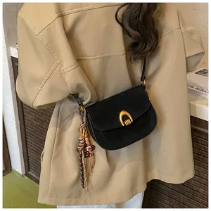 Detail of a black matte saddle bag featuring a gold U-shaped buckle and tassel charm
