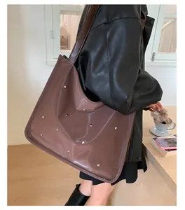 Detail of a brown glossy tote bag with silver heart rivets and wide shoulder strap