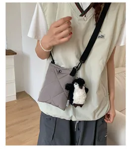 Détail d'un sac bandoulière gris matelassé avec un charme pingouin et sangle tissée