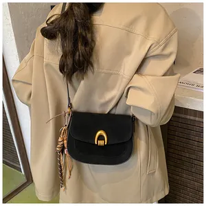 Detail of black suede shoulder bag with gold horseshoe buckle and woven strap ornament