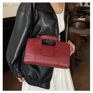 Detail view of dark red crocodile pattern handbag with gold chain on model in cafe