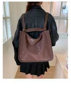Close-up of brown glossy tote bag featuring silver studs and slim leather shoulder straps