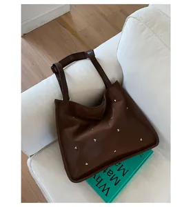 Detailed close-up of dark brown tote bag with silver heart studs on a white sofa