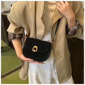 Detail of black crossbody saddle bag with gold metal buckle and matte texture on model