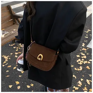 Close-up of a dark brown suede saddle bag featuring a gold U-shaped buckle and woven charm