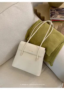 Detail of cream faux leather tote bag with gold logo and decorative beaded straps