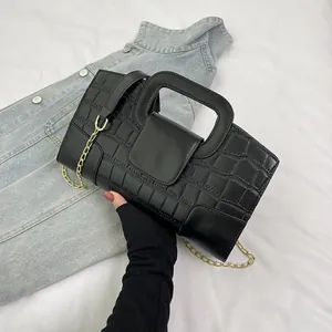 Detail of black crocodile texture leather bag with rectangular handle and gold chain strap